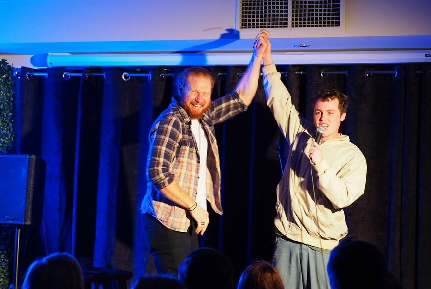 Two people on a stage giving each other a high five, one also holding a microphone.