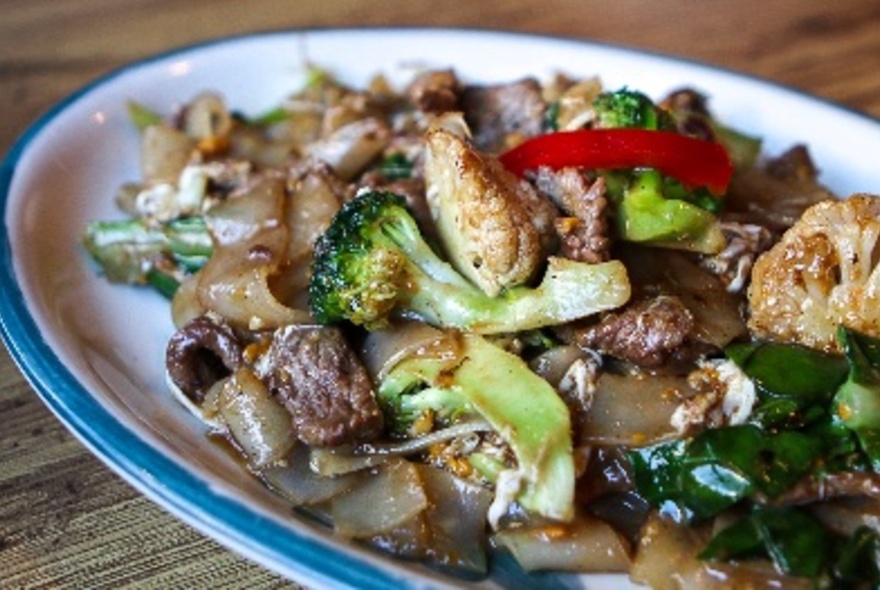 A plate of Thai noodles with meat and vegetables.