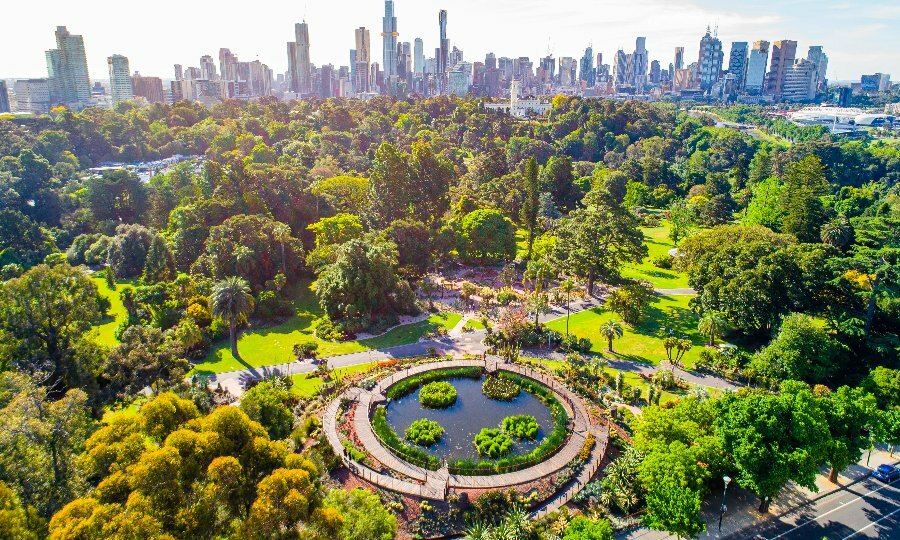 An aerial view of a big park featuring a pool surrounded by trees and the city skyline in the background
