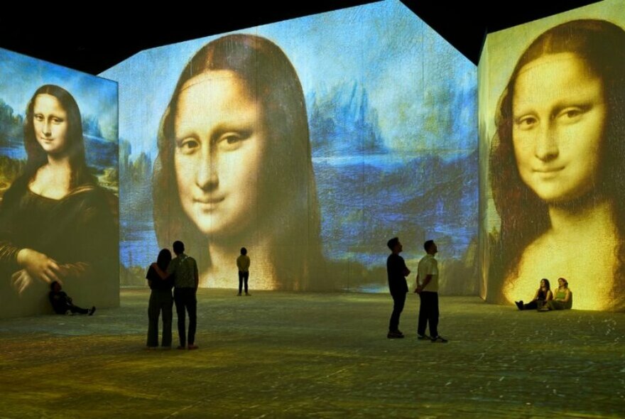 People in an immersive gallery of oversized depictions of the Mona Lisa.