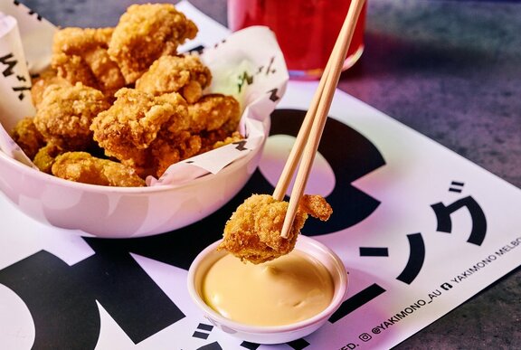 Someone dipping a piece of chicken karaage into a pot of mayo.