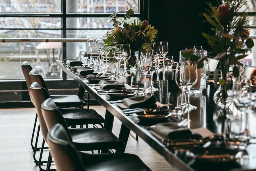 A long table with multiple place settings, floral table decorations and leather chairs.