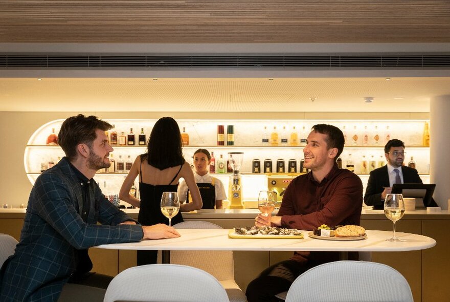People chatting in a modern bar with backlit shelves of bottles.