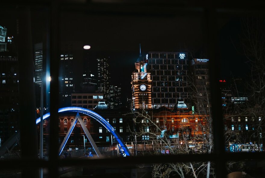 A view of Flinders Street station at night through a metal framed window.