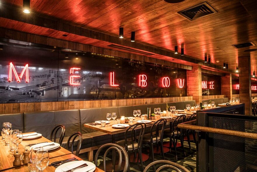 The interior of a restaurant with bentwood chairs and a neon MELBOURNE sign on the wall. 