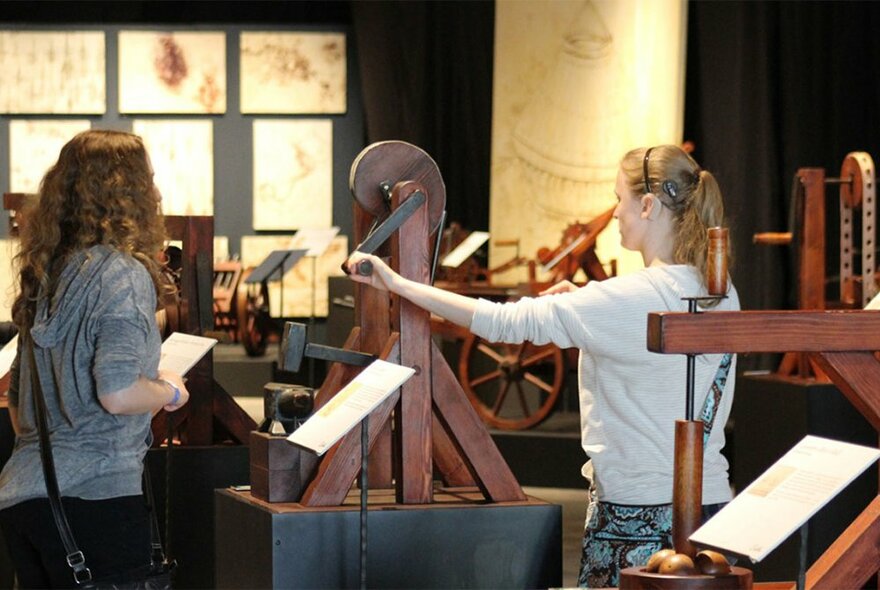 Two women trying out Leonardo da Vinci's wooden machines. 