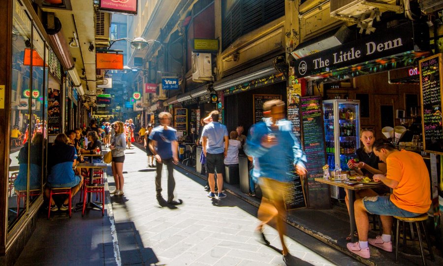 Narrow city laneway filled with shops and people eating at pavement cafes.