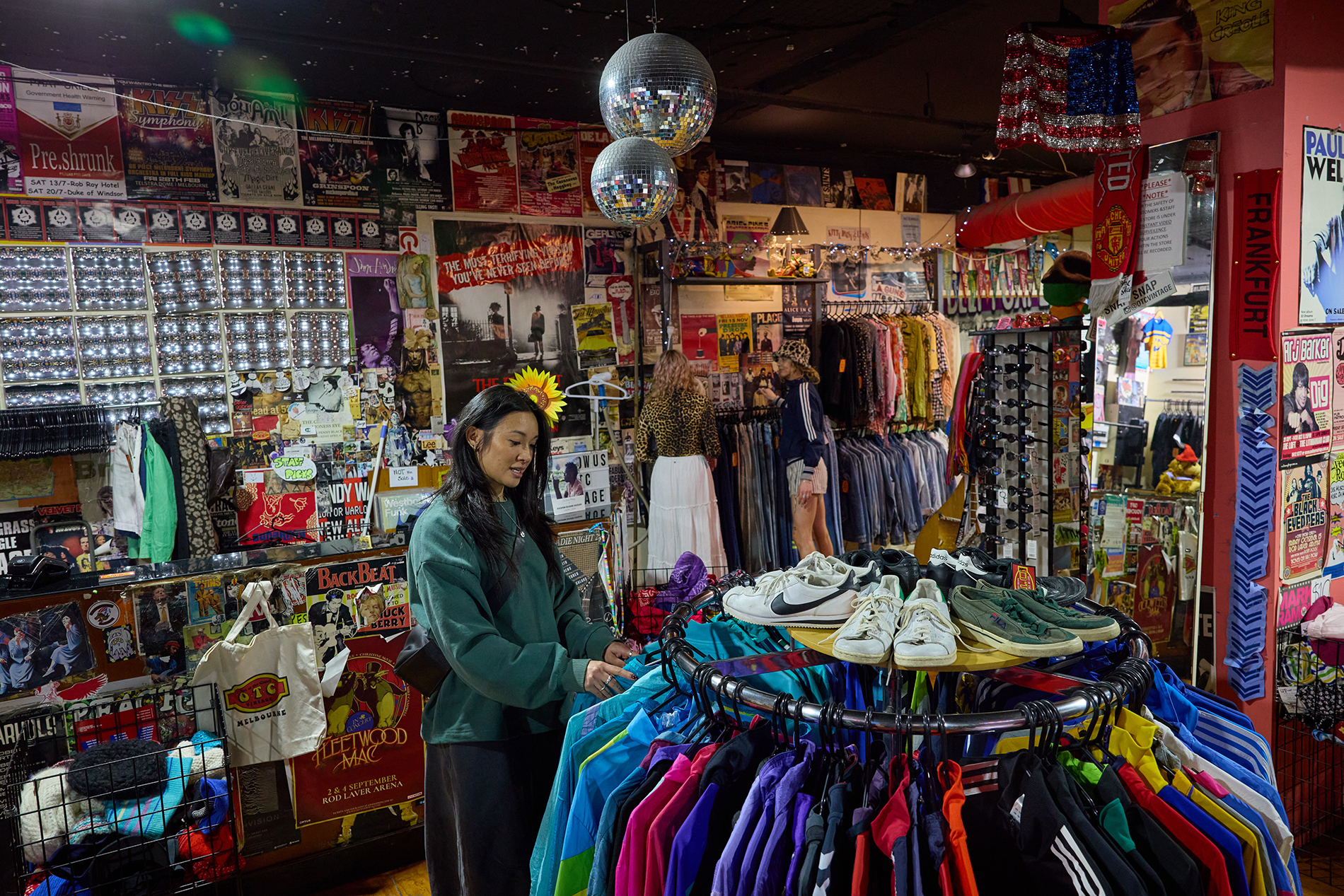 A woman browsing a rack of colourful jackets in a vintage shop with disco balls.
