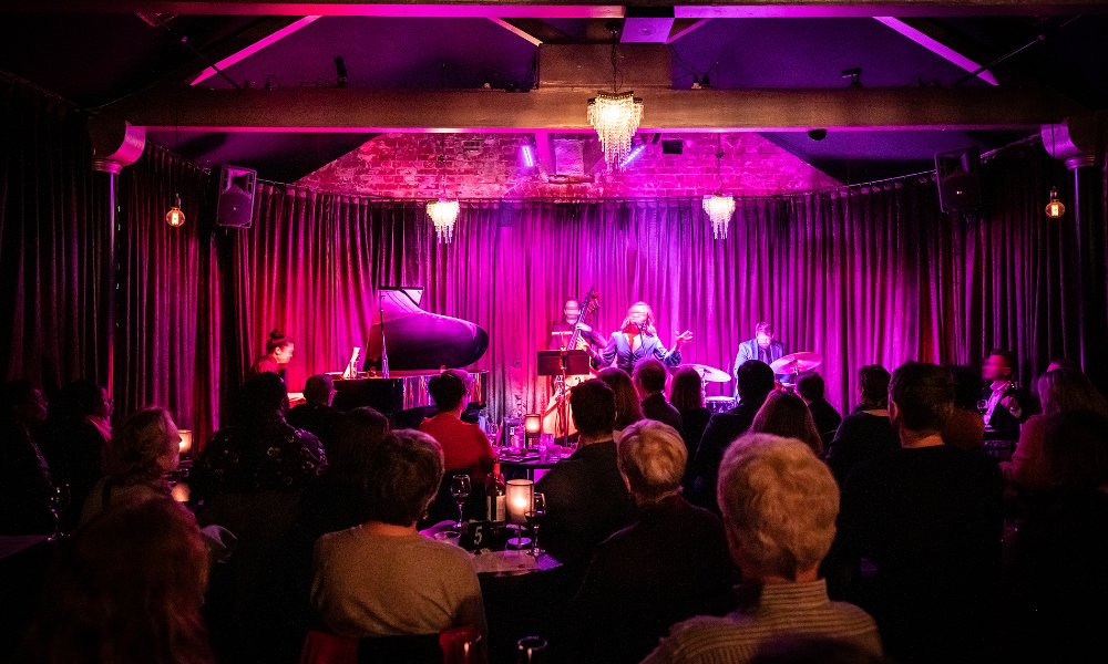A band performing under pink lights to a crowd.