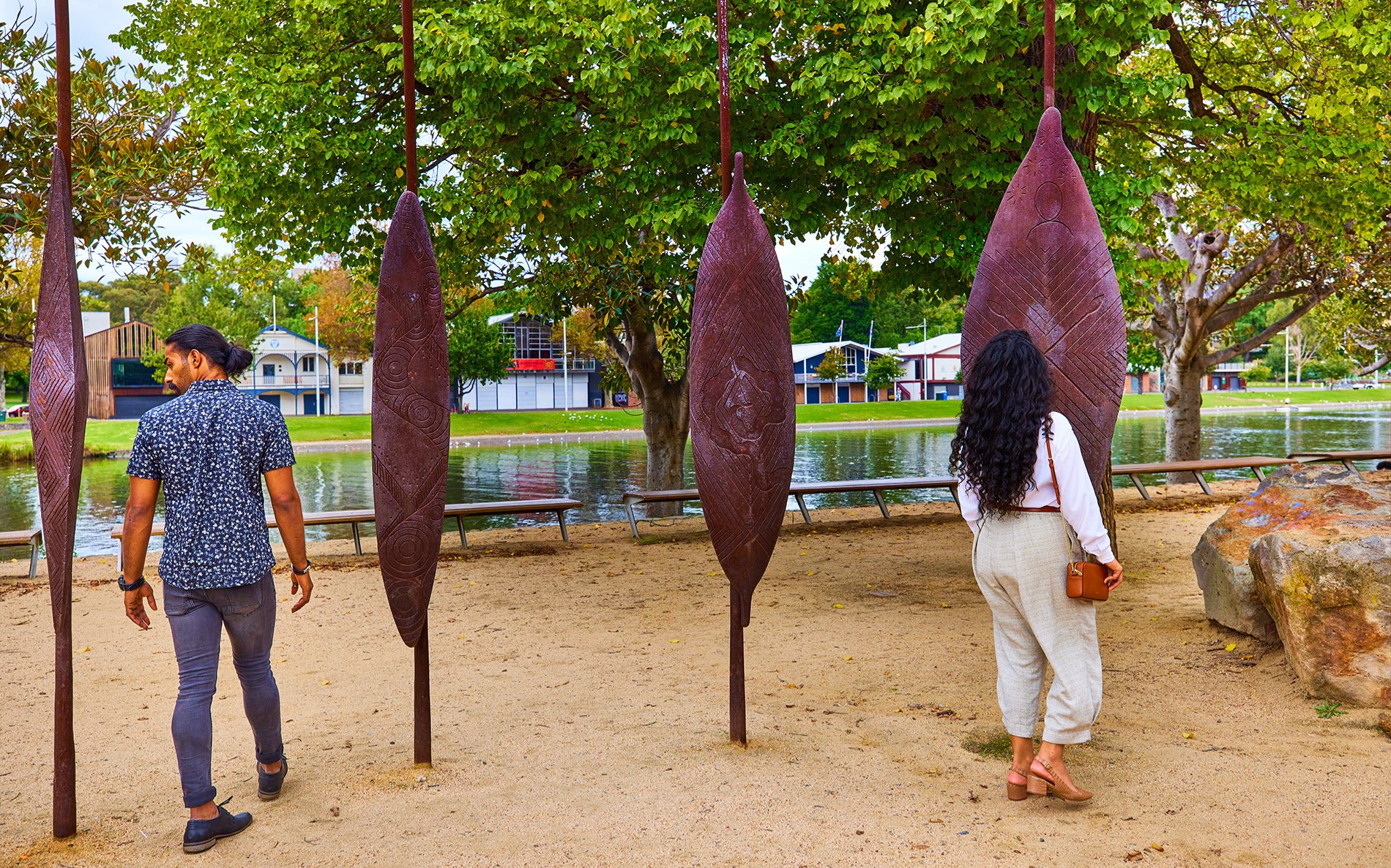A couple walking through an art installation with large shield sculptures by the river.