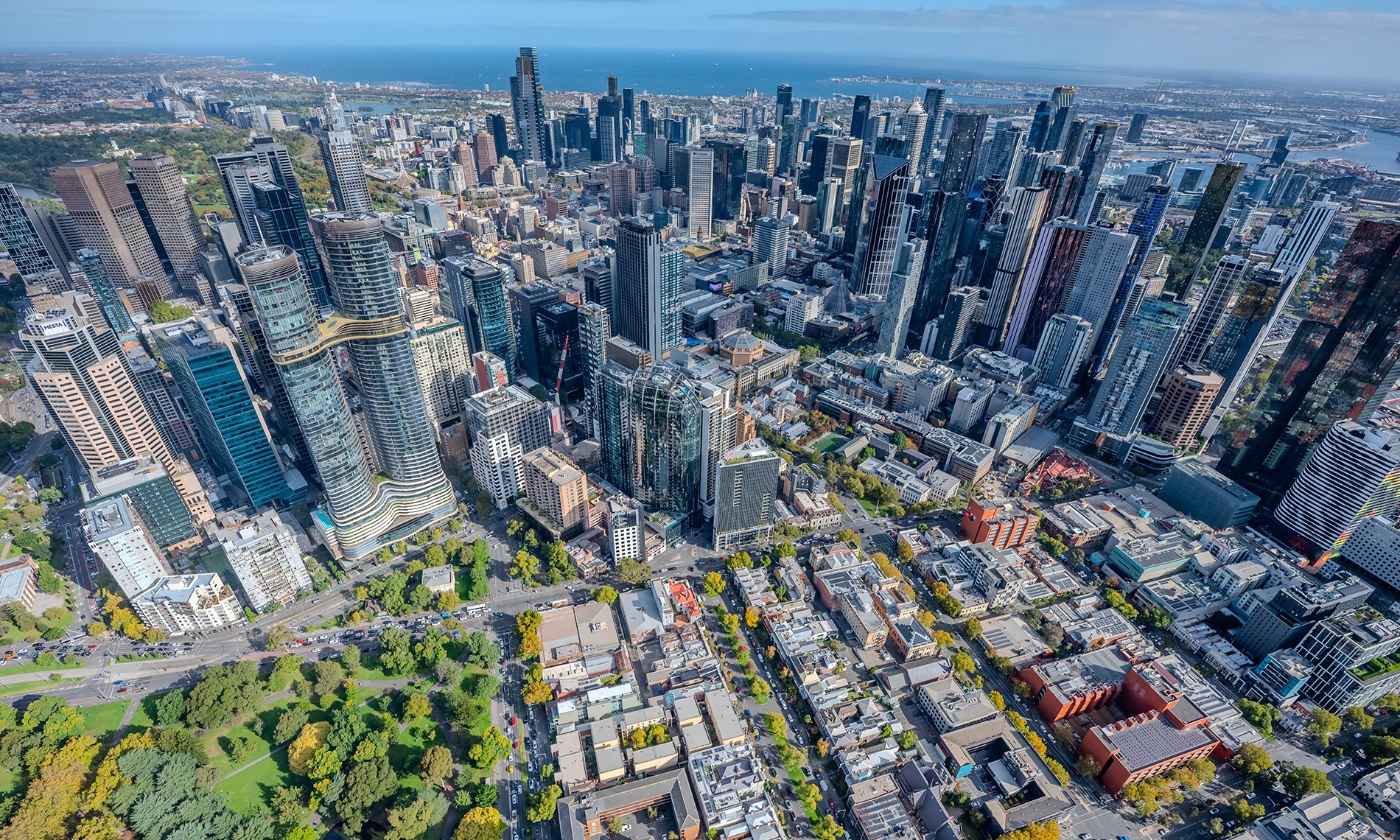 An aerial view of a city with a park, skyscrapers and ocean.