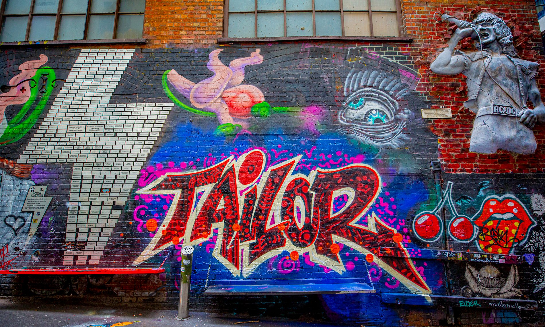 A wall of street art including a concrete bust of a singer, cherries and a lightning bolt.