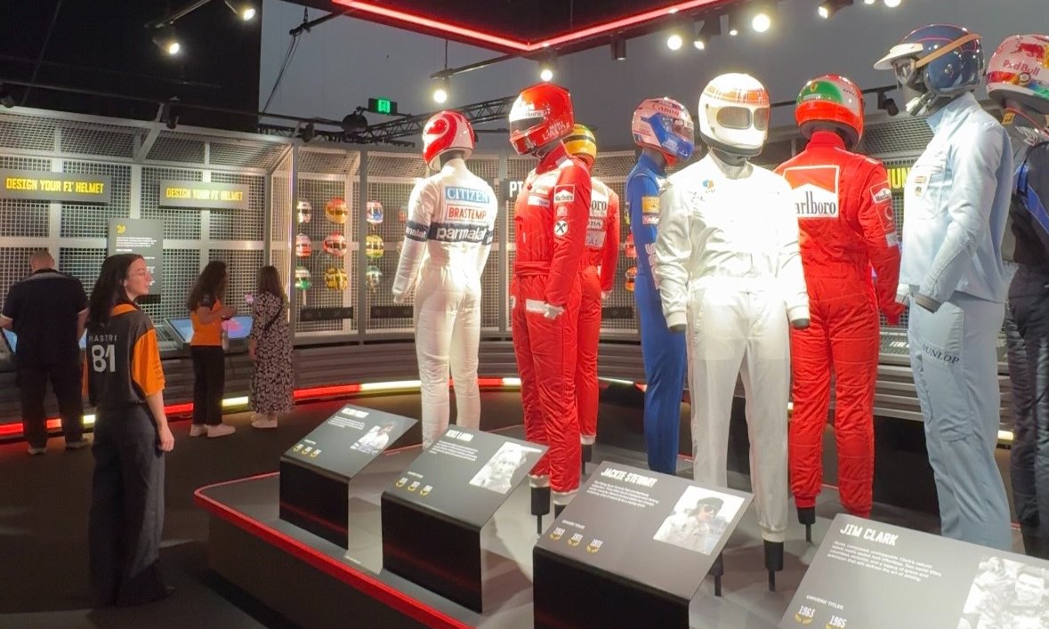 A woman looking at a display of Formula 1 racing suits in an exhibition.