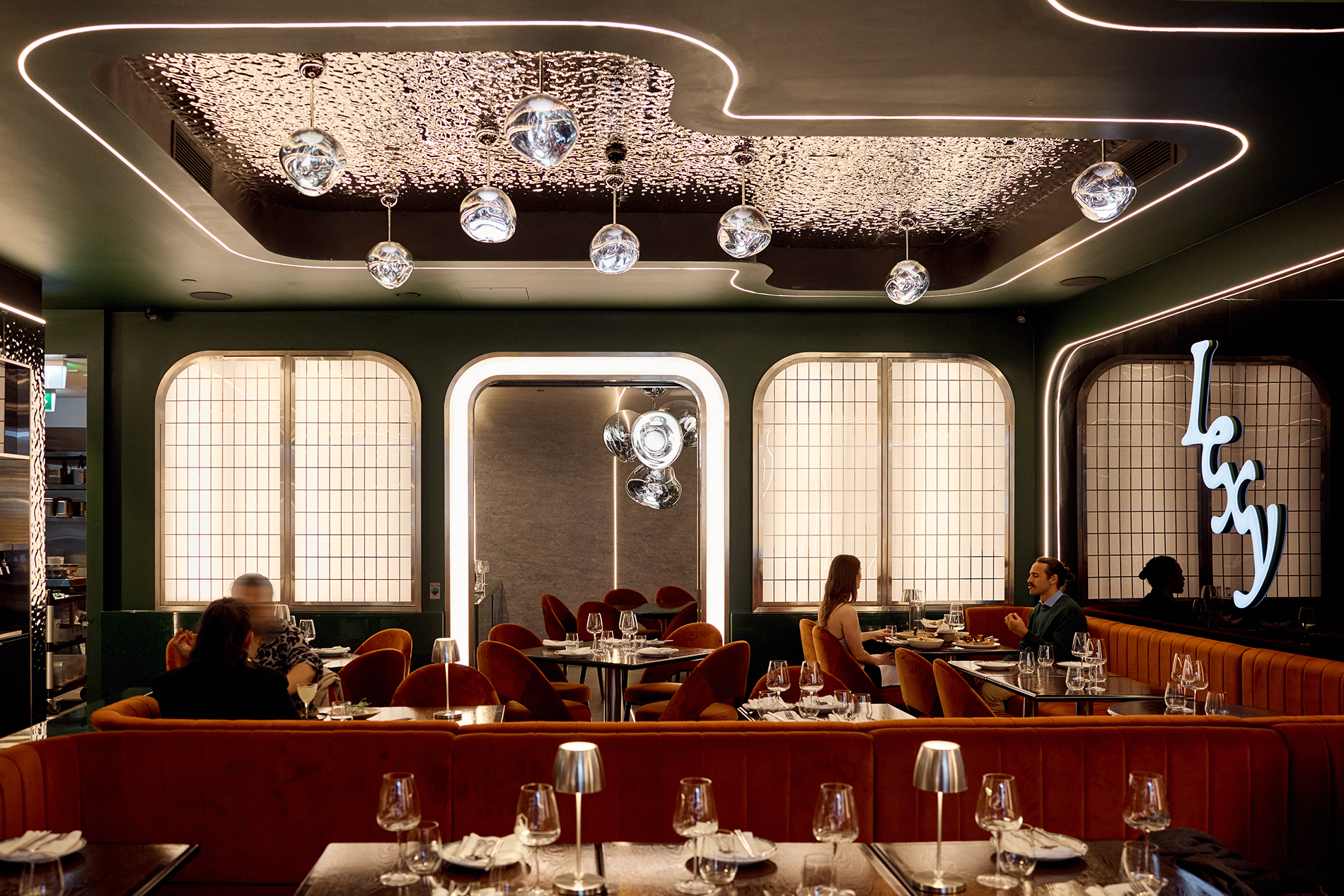 A modern restaurant with glam light fixtures and velvet booths.