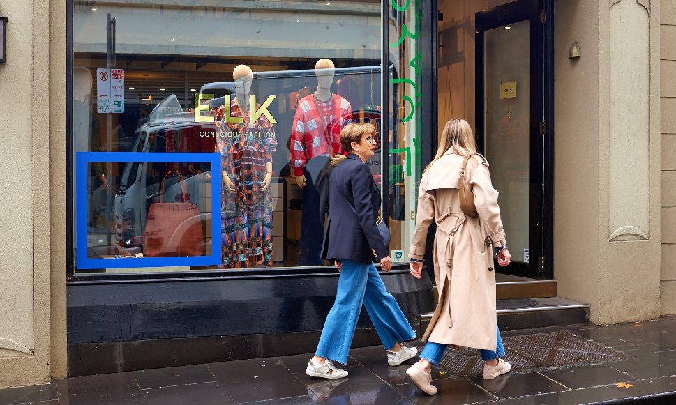 Two women are walking into a clothing shop. 