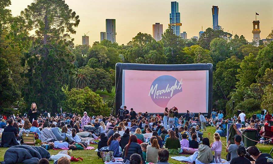 Crowd of people seated on the grass watching the Moonlight Cinema in the Royal Botanic Gardens.