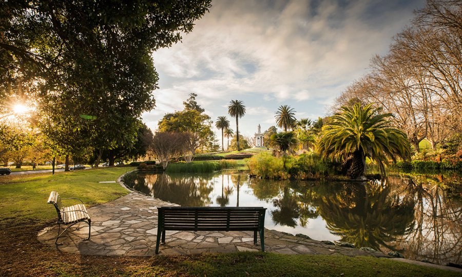Empty park benches next to a pond at dusk.