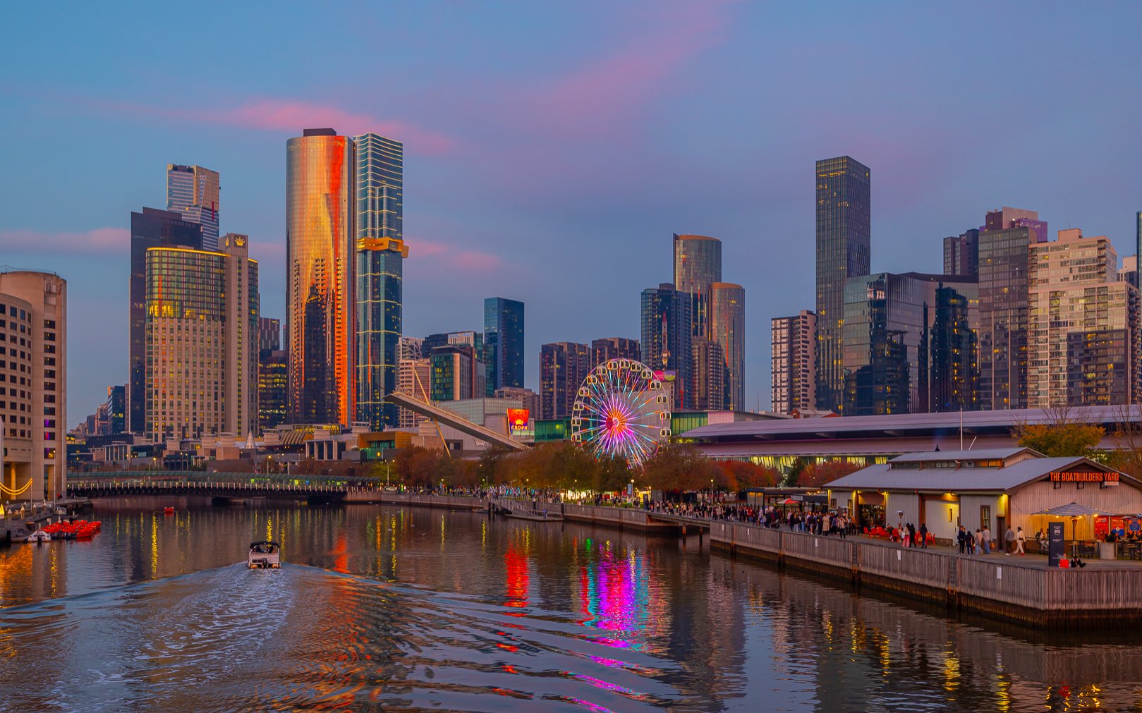 A Ferris wheel in the city at sunset with colourful reflections on the river.