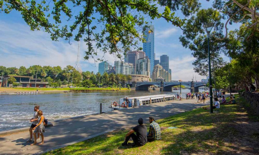 People sitting in the shade next to the Yarra River in the city.