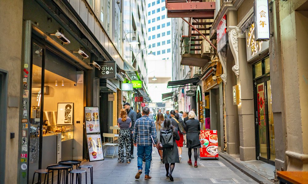 People walking past cafes in a busy laneway. 