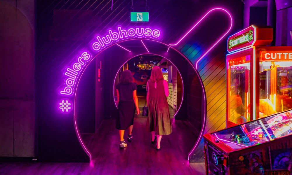 Two people walking through the entrance of a bar with neon signage.