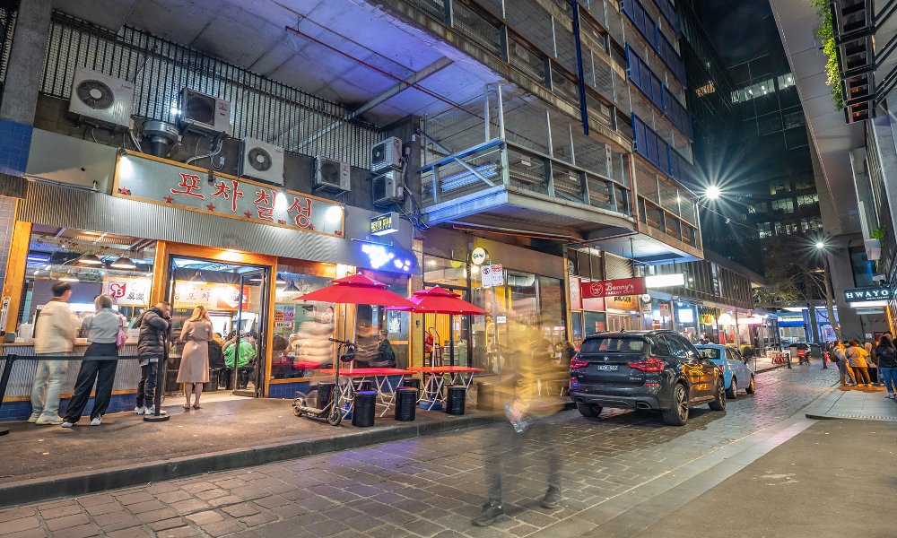 Crowds outside restaurants in a city laneway at night.