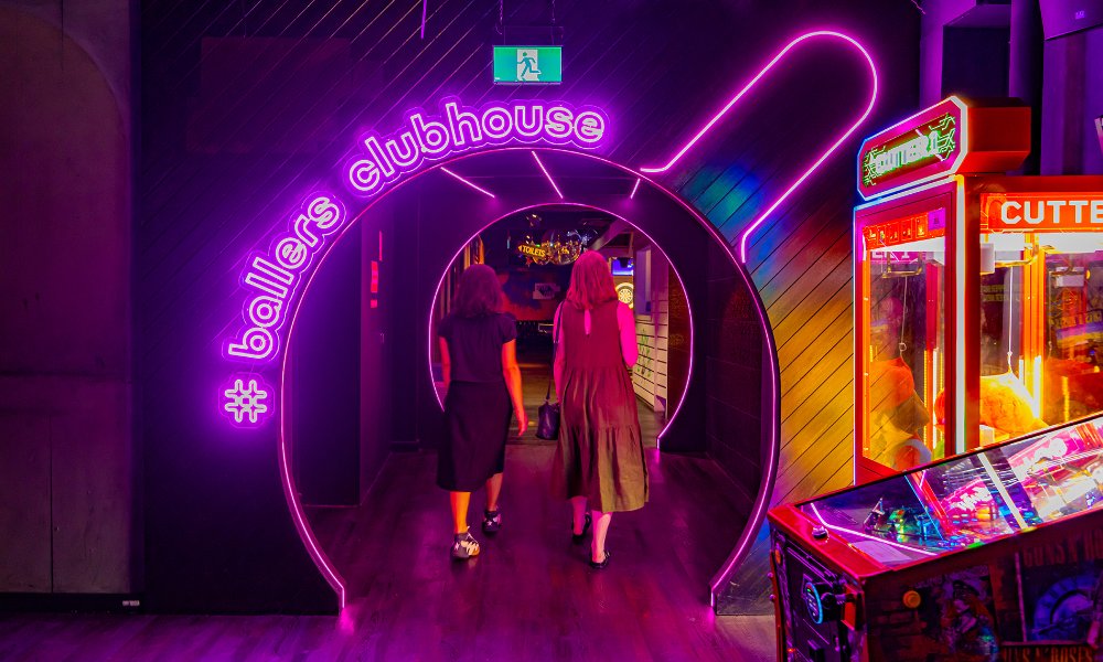 Two friends walking through a neon lit doorway shaped like a table tennis paddle.