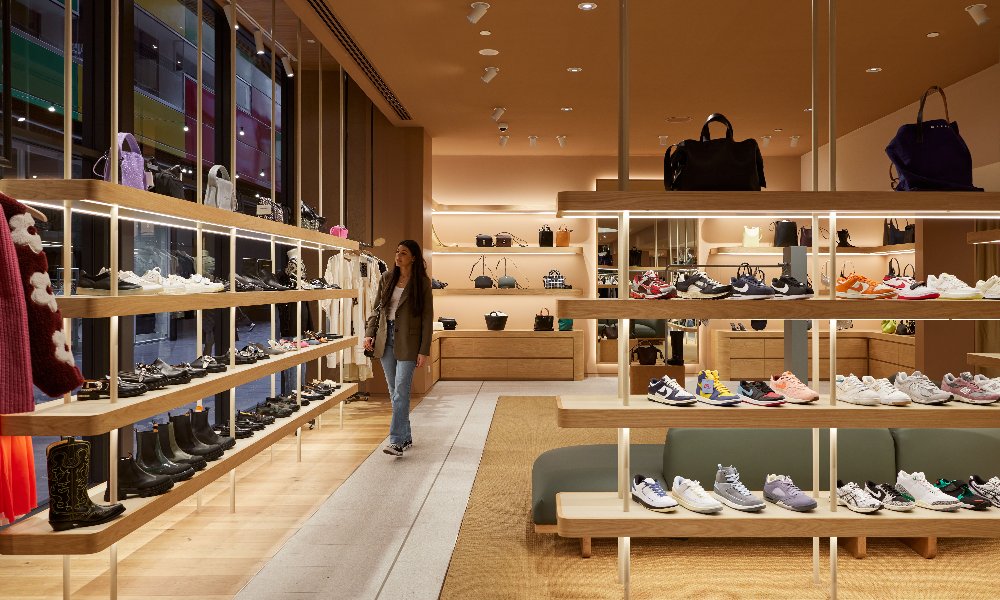 A woman in a warmly lit clothing store with shoes on display.