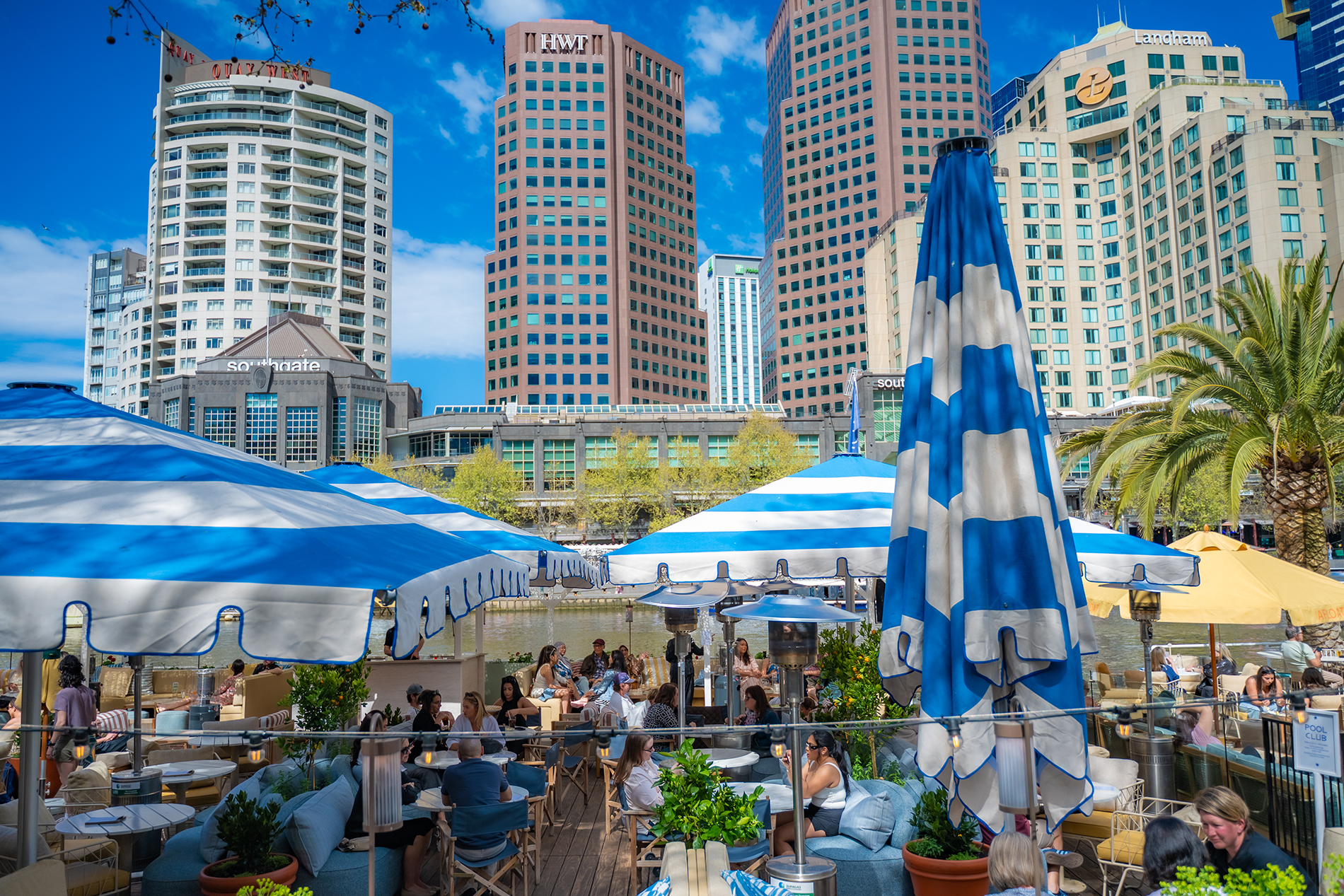 An outdoor restaurant on the river with blue and white umbrellas.