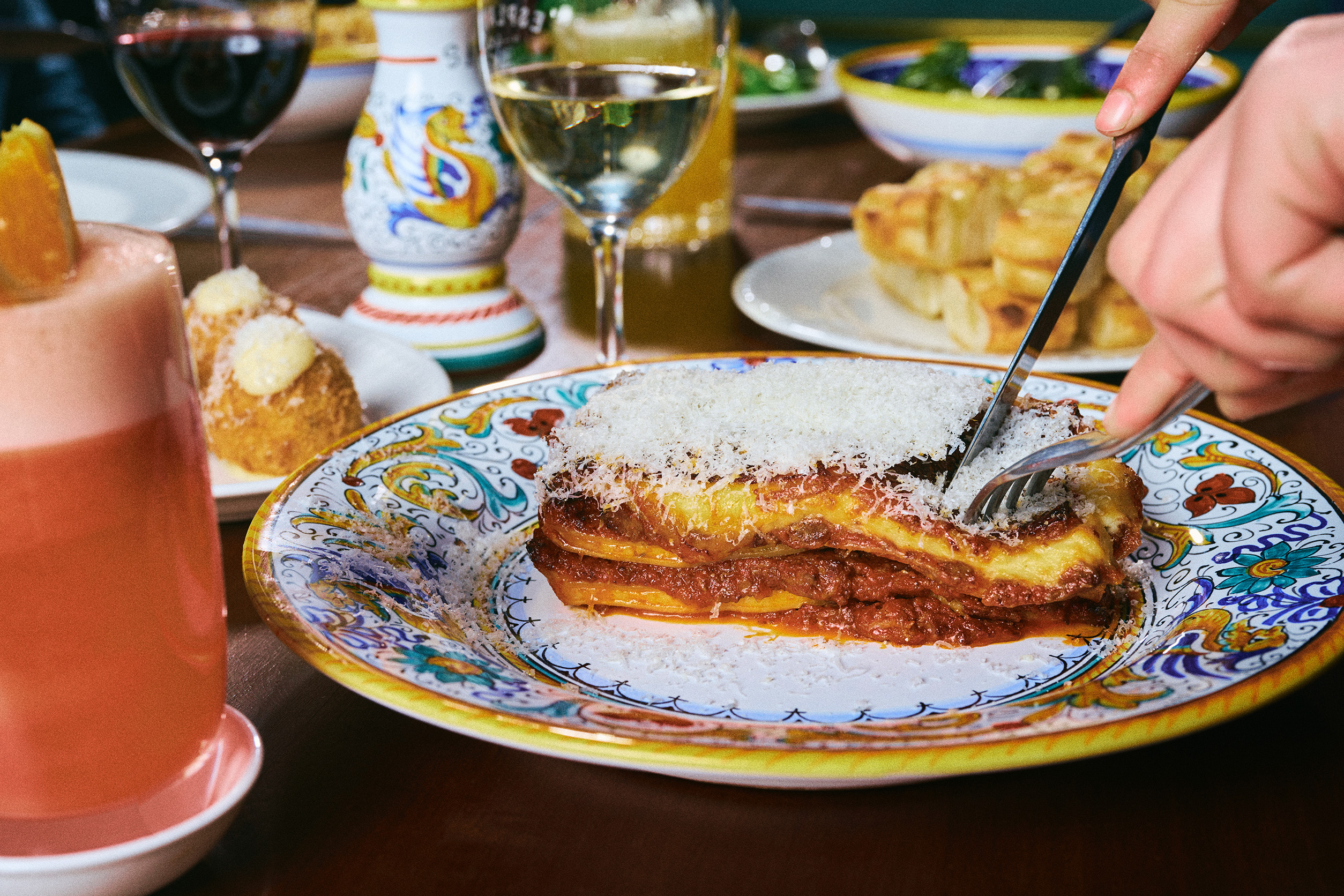 A person is cutting into a slice of lasagne on a colourful plate