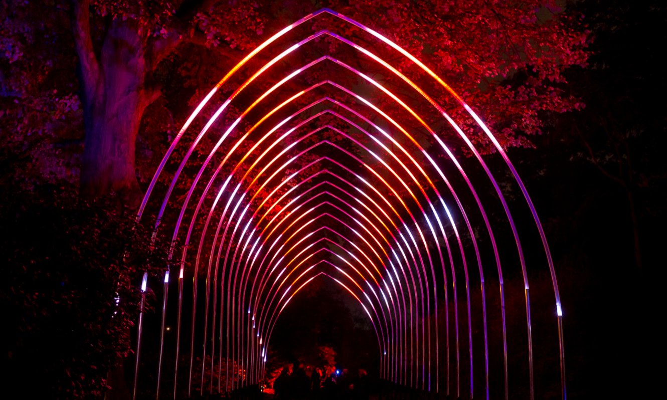 A glowing archway of red lights in a garden at night.