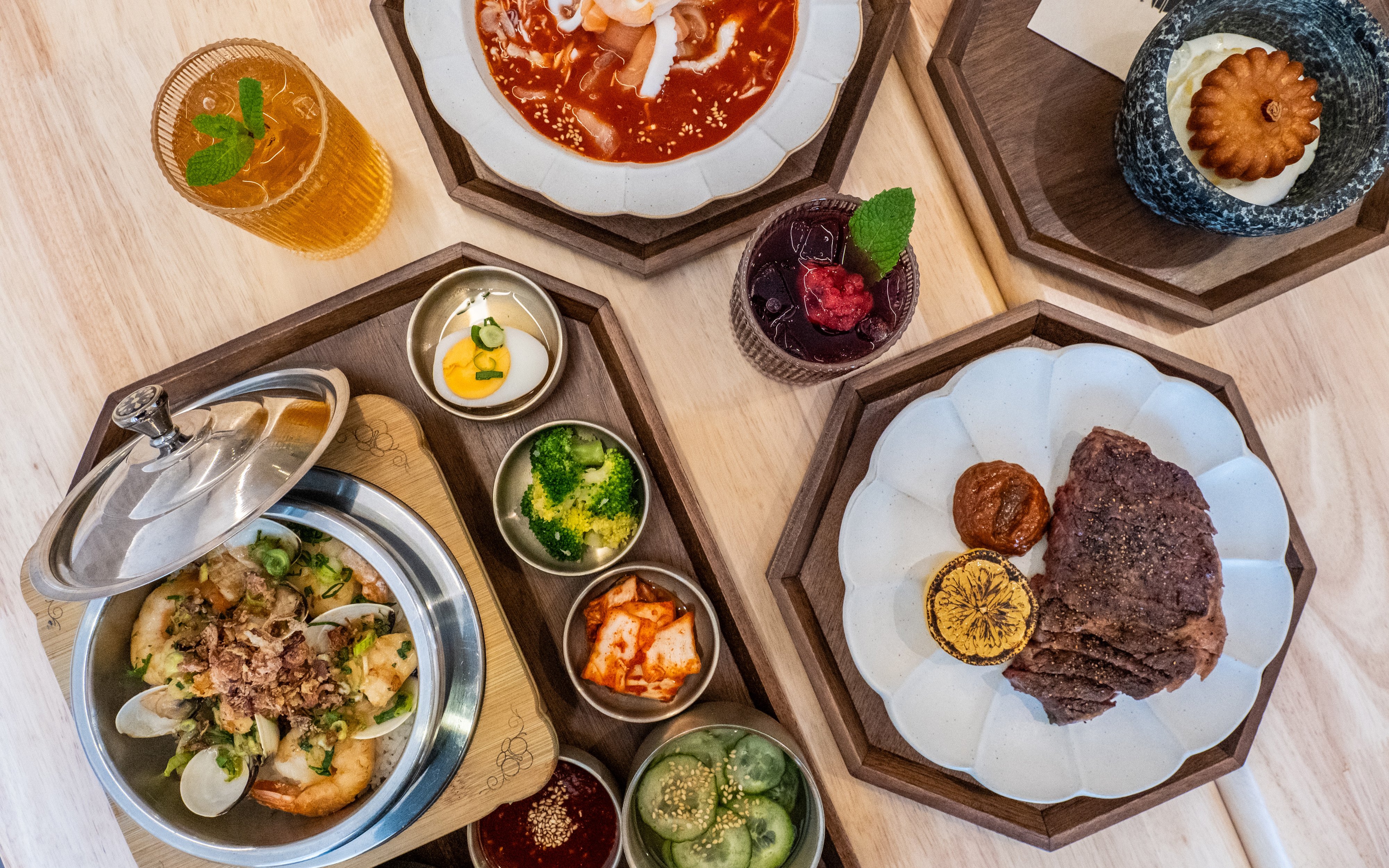 Korean dishes served on plates and in a steel pot with an assortment of small sides and drinks.