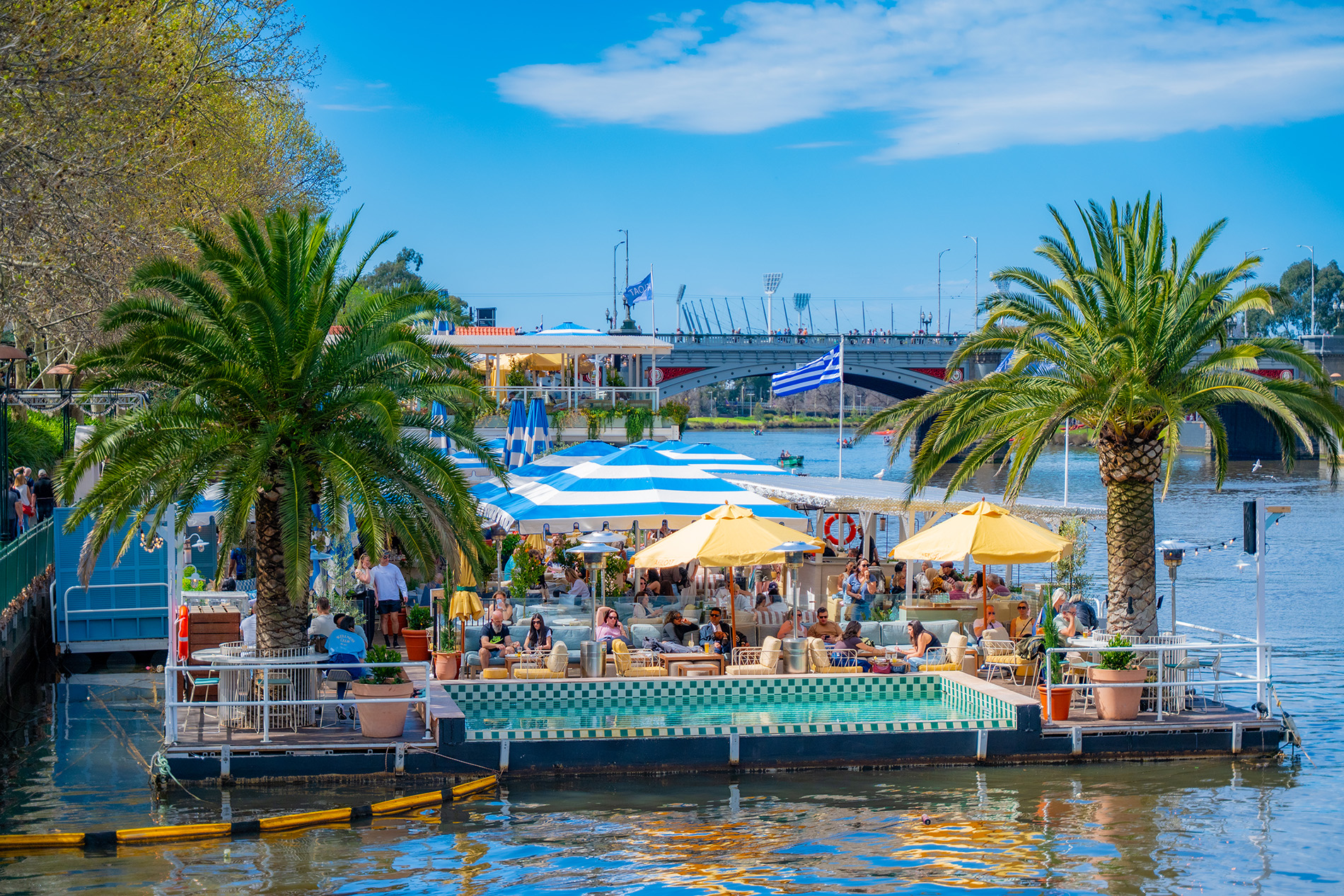 A floating bar with a pool and palm trees, on the river in the city on a sunny day.
