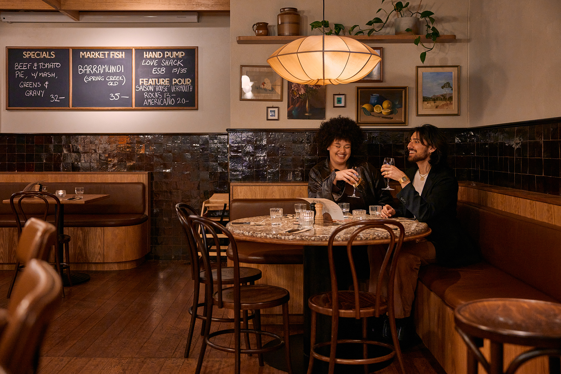 Two friends sitting at a pub table sharing a wine. 