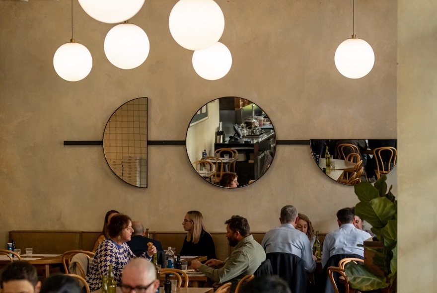 Patrons at an Italian restaurant in Southbank, Melbourne with circular lights and round mirrors on the back wall.