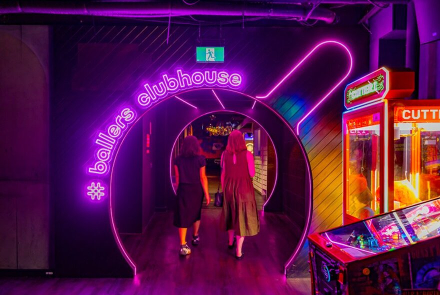 Two women walking into room under big neon signage and arcade games.