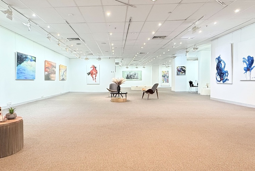 Long view of a stark white gallery space with a beige floor and artwork hanging on the walls.