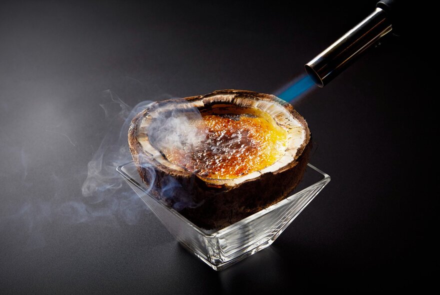 Blowtorch searing a caramellised dish of food.