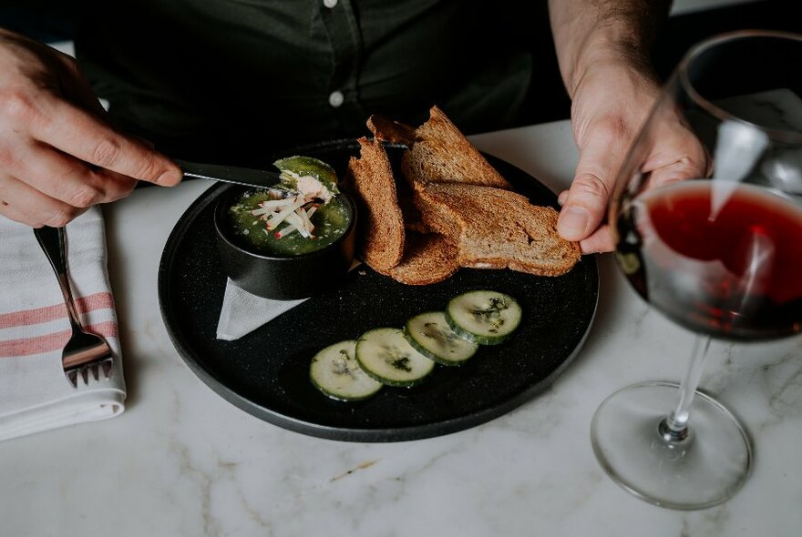 A diner with a plate of trout rillettes and a glass of red wine. 