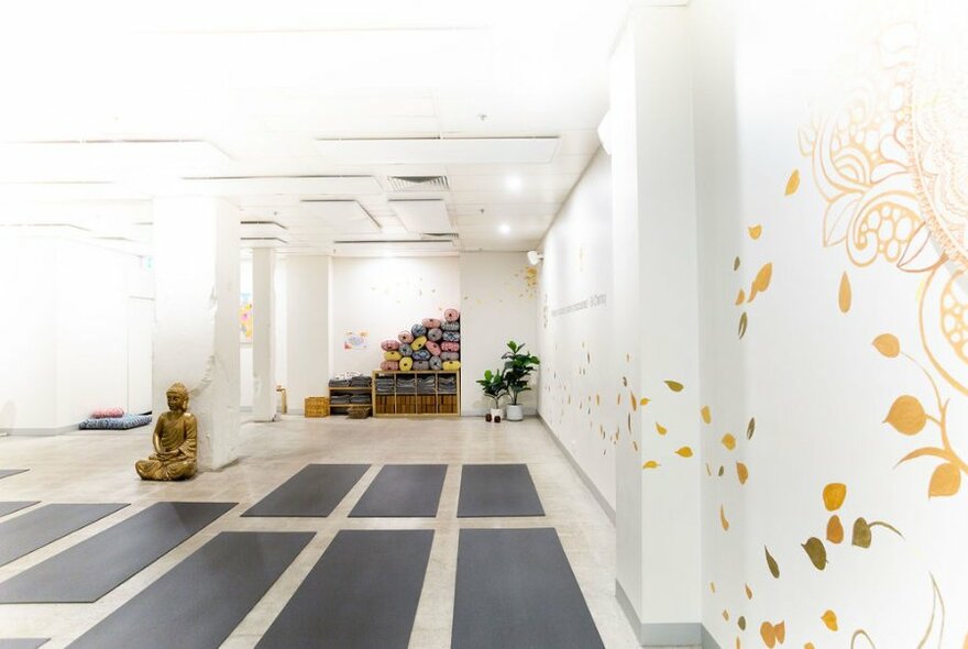 Interior of a yoga studio with several floor mats, yoga props along the back wall and a decorated side wall.