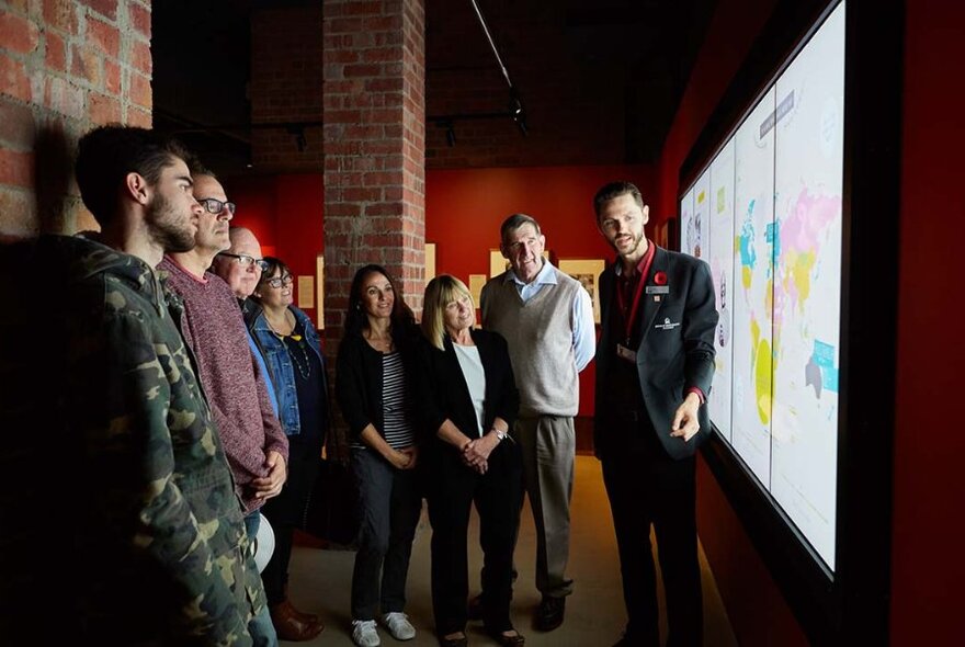 A guide talking to a group of people inside the Shrine in front of a display screen.