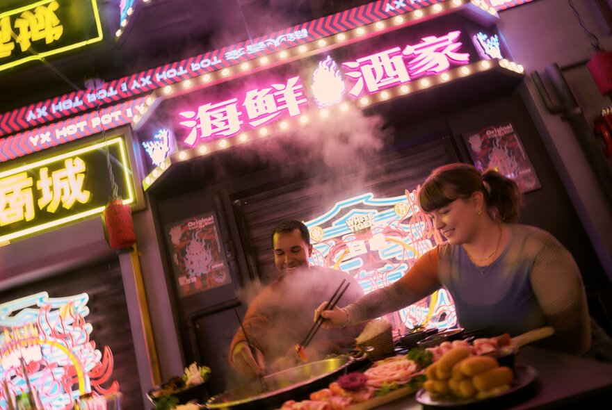 Two people eating hot pot under neon signs.