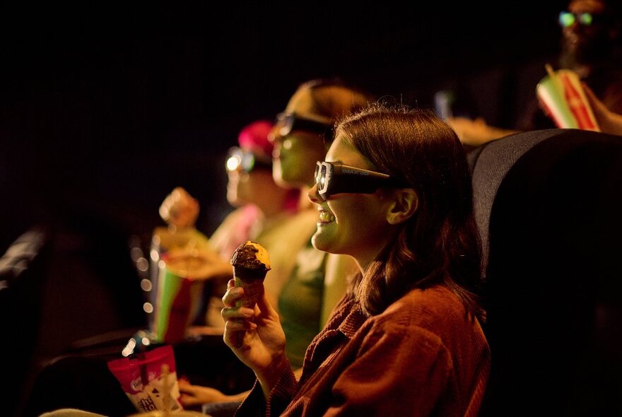 People at IMAZ viewing a movie through special glasses, eating snacks and smiling.