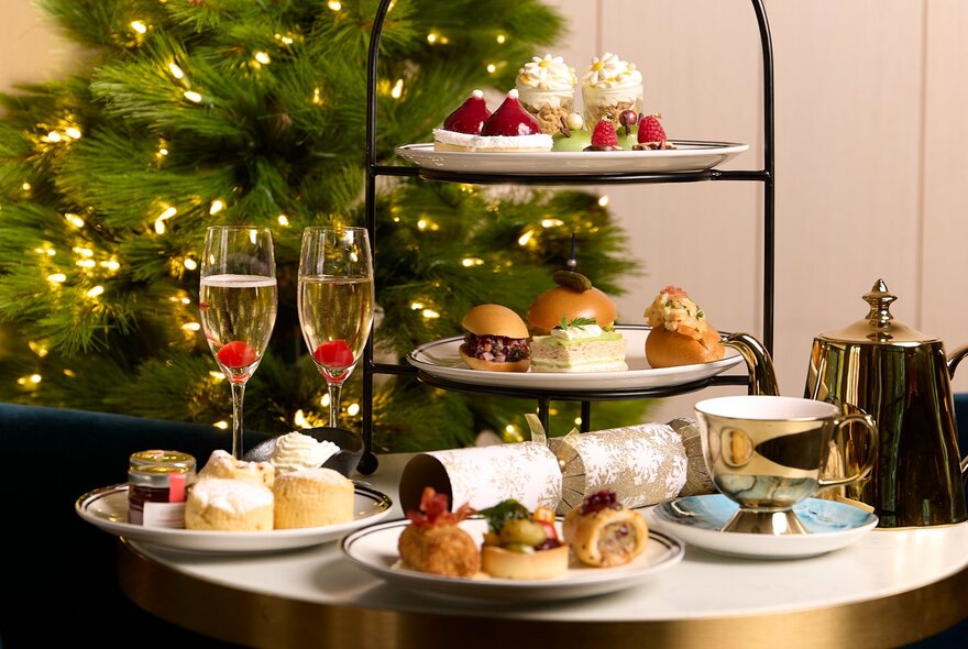 A festive-themed high tea with a three-tier stand of savoury and sweet food, two flute glasses of sparkling wine and a silver pot of tea.