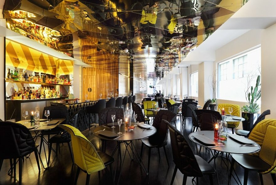 Interior of Adelphi Hotel restaurant with round tables set for two or four, a reflective ceiling and a golden coloured bar on the left side.