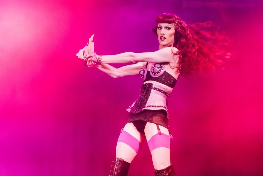 Dancer wearing pink stockings and Amazonian underwear, under pink lighting.