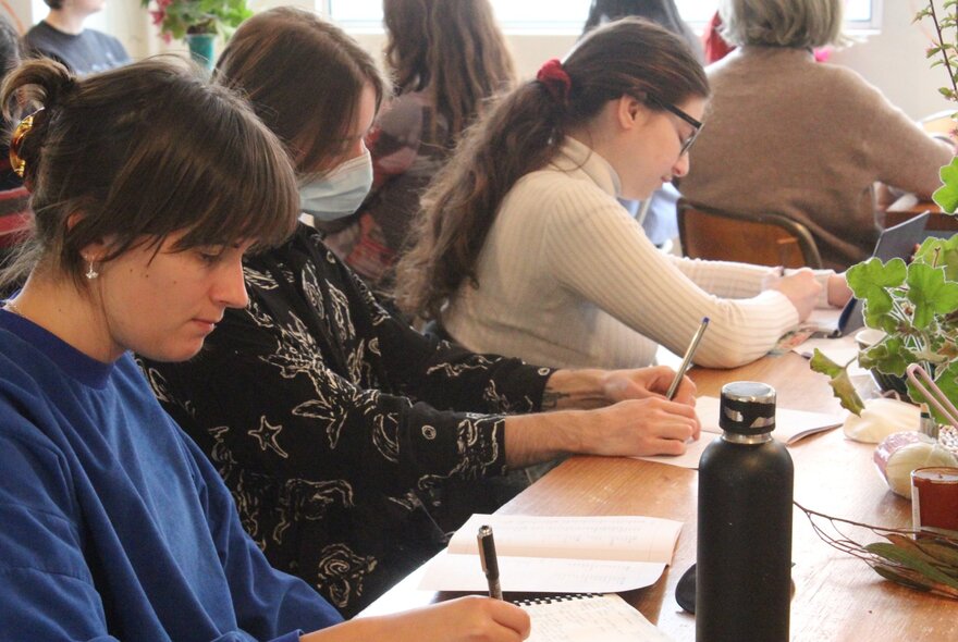 People seated at a table, using pens and notebooks to write.