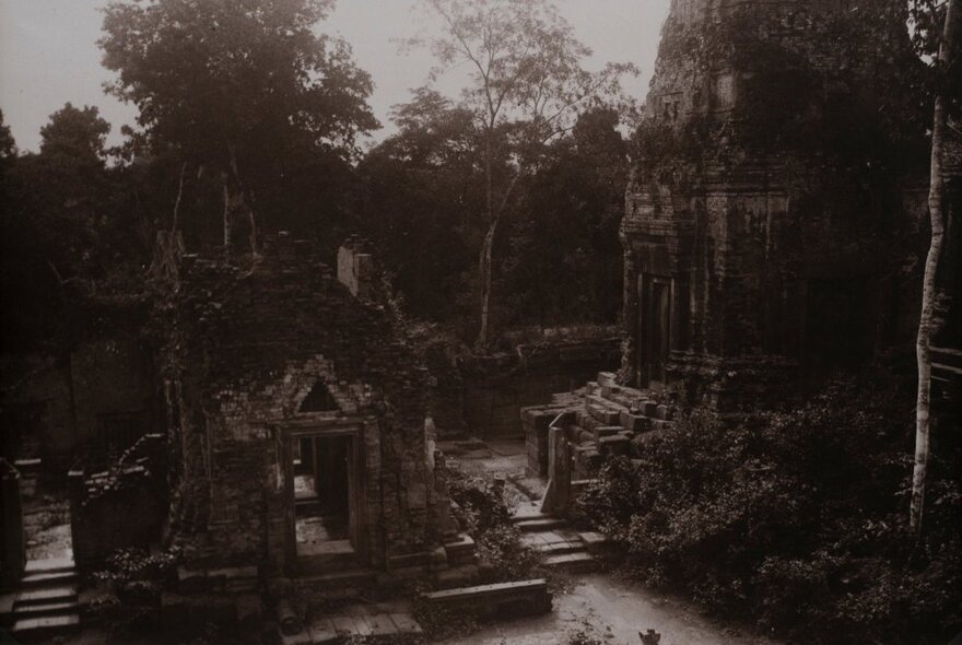 Dark black and white image of a ruins amongst trees.