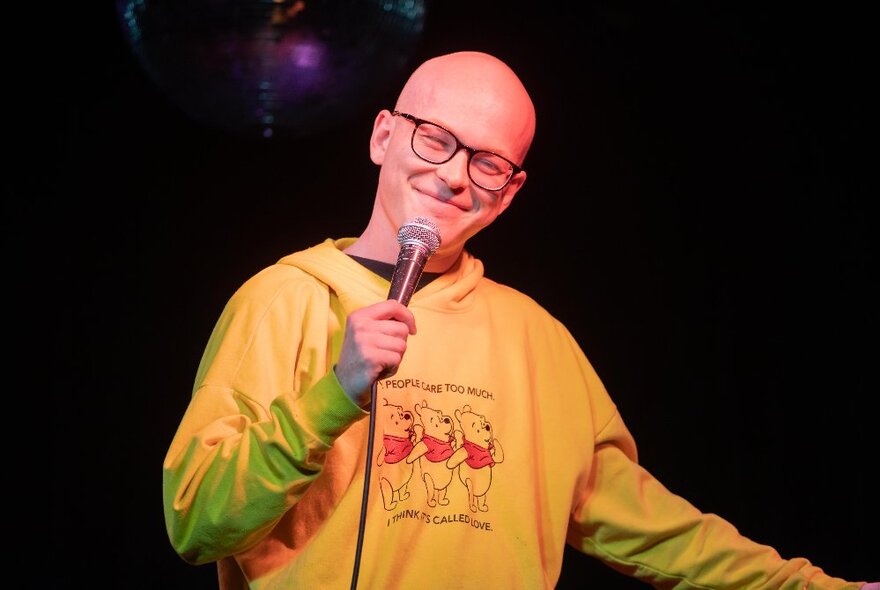 Comedian Danny Sewell, a young smiling man performing stand-up comedy on stage, holding a microphone.