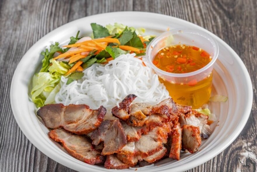 A plate of roast pork, rice noodles, salad and dipping sauce.